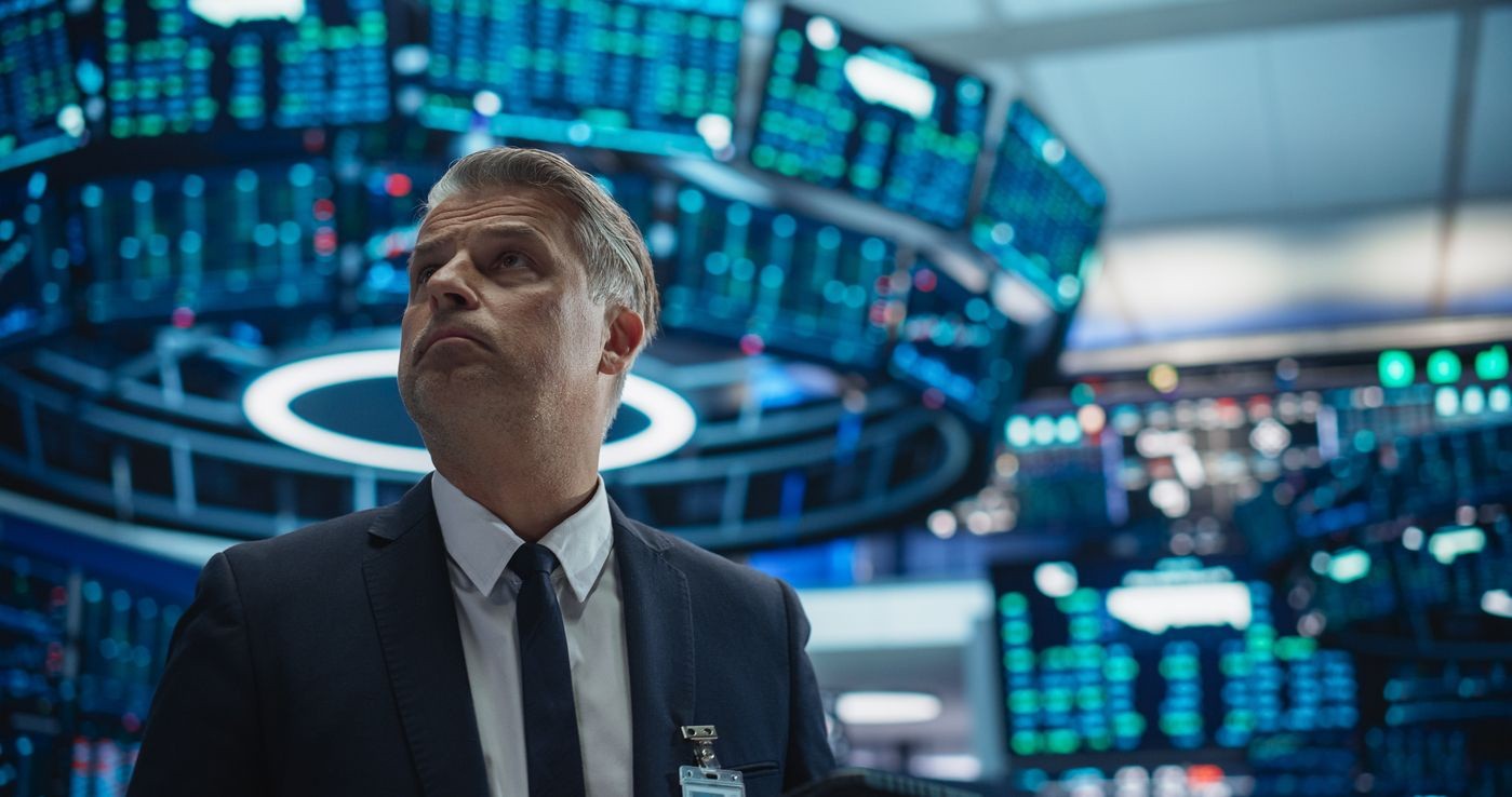Businessman monitors digital stock market displays on a busy trading floor.