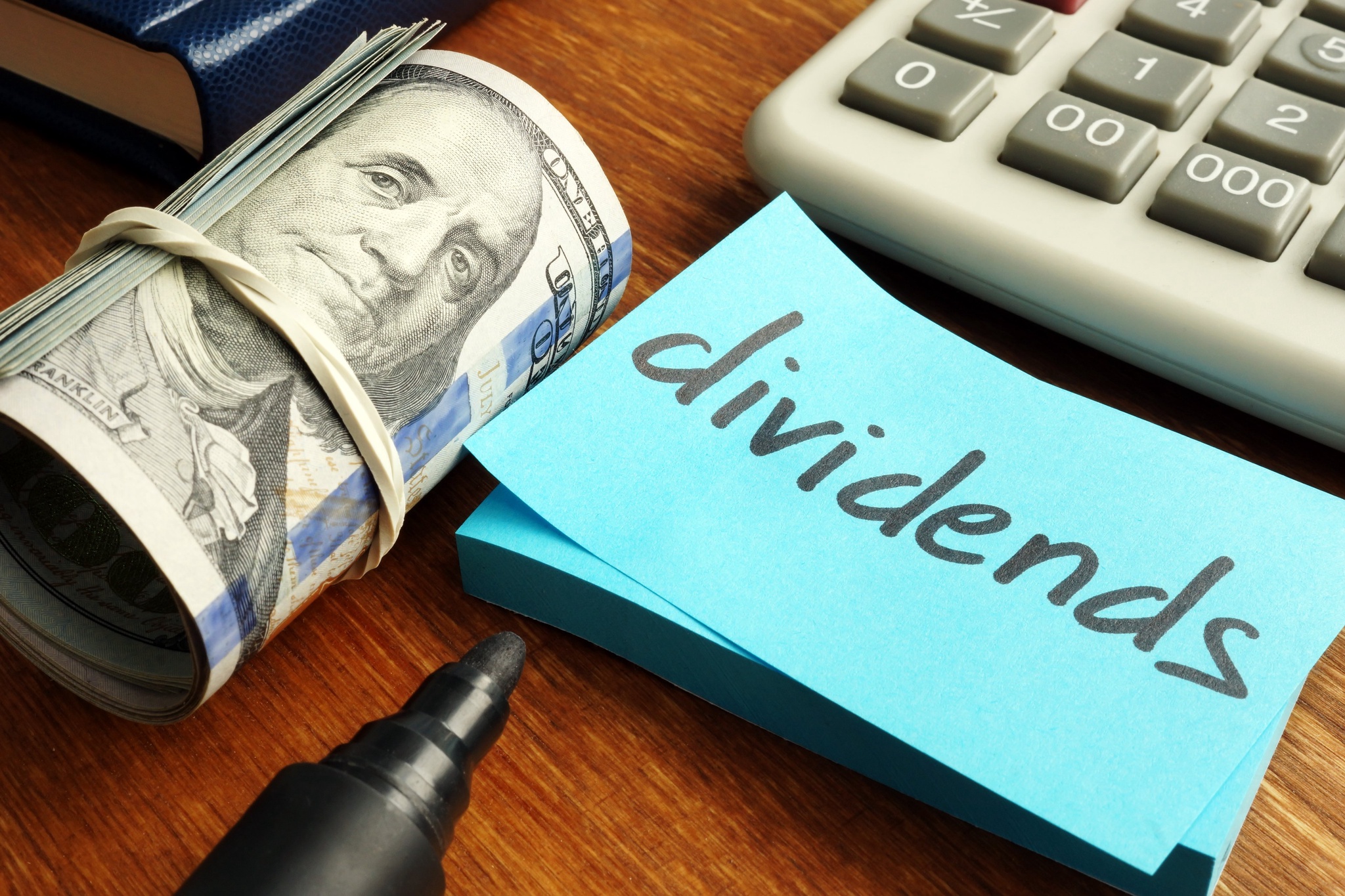 Sticky note with dividends written on it next to a roll of money. 