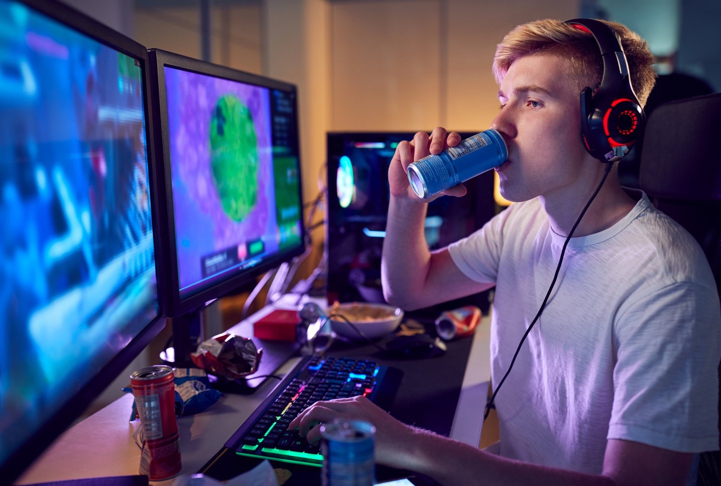 A seated person taking a sip from an energy drink while gaming on their personal computer.
