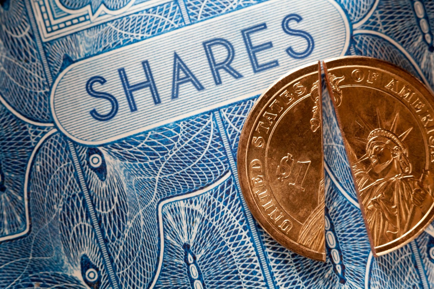 A U.S. dollar coin split in half that's been set atop a paper stock certificate for shares of a public company.