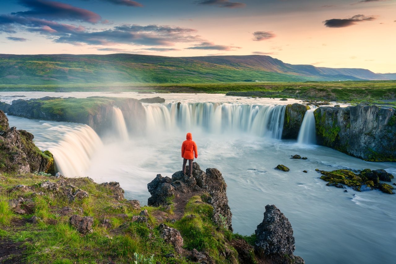 A person standing on a cliff overlooking a large waterfall system.