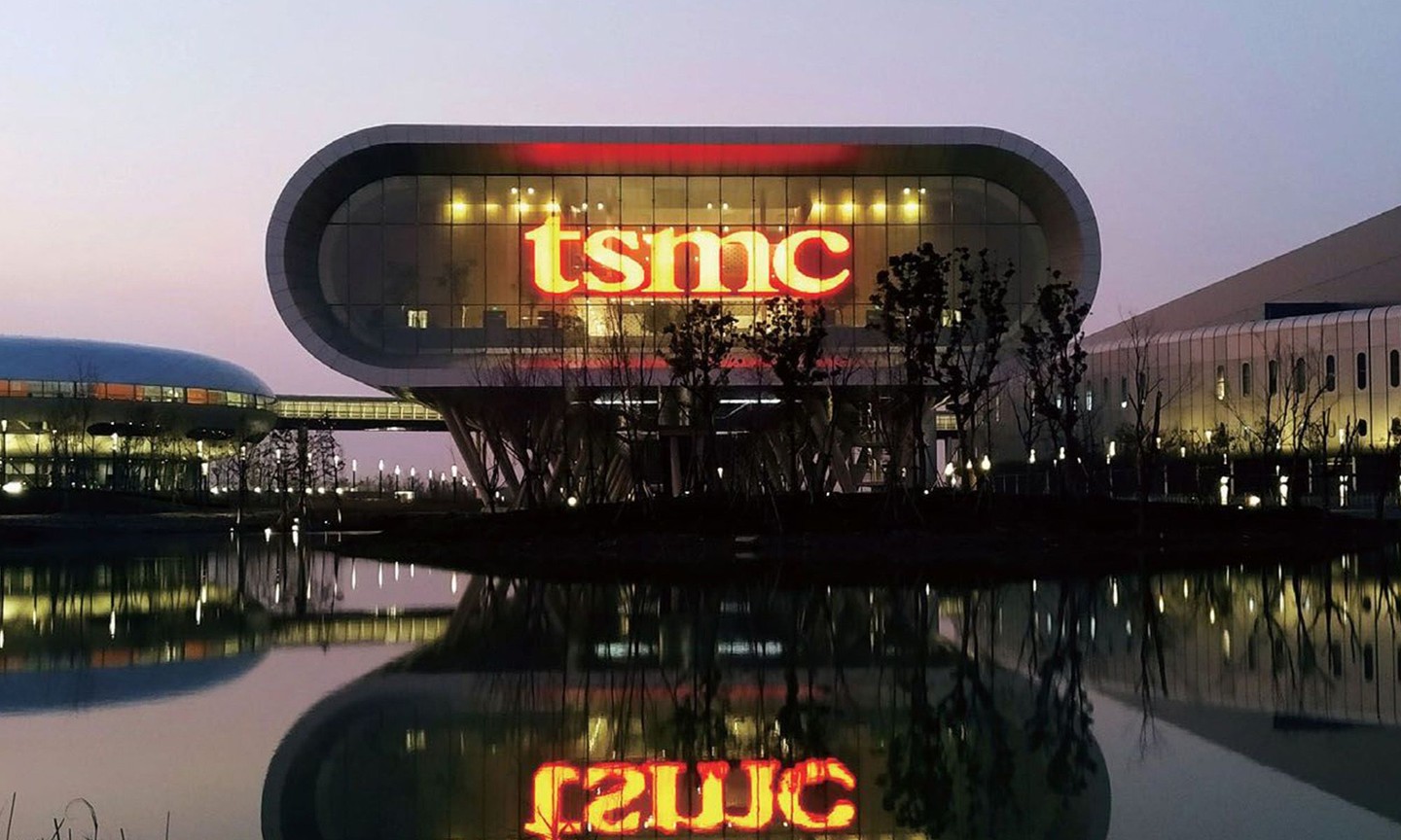 TSMC headquarters at dusk with glowing red logo reflected in a calm pond.